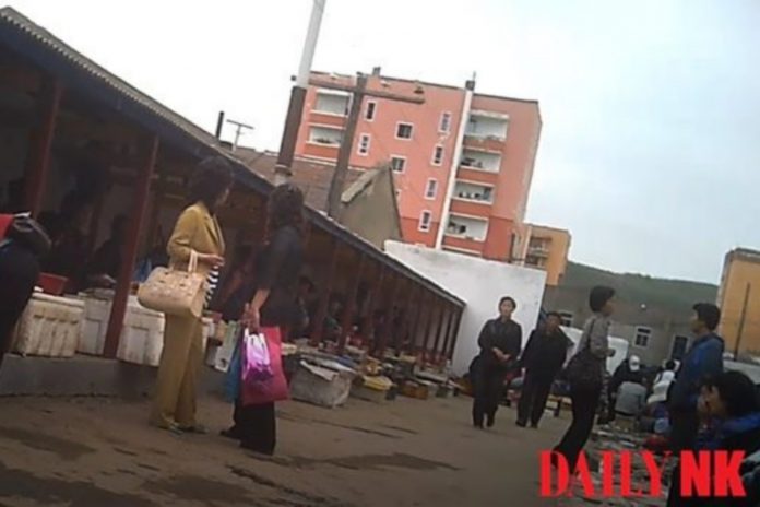 A market scene in North Korea with two women in the foreground, along with other people walking in background.