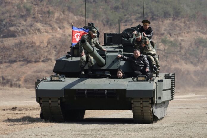 Kim Ju Ae drives a new-model North Korean tank during a combined arms tactical exercise at Pyongyang's 60th Training Base, March 19, 2026, as Kim Jong Un and military officers look on