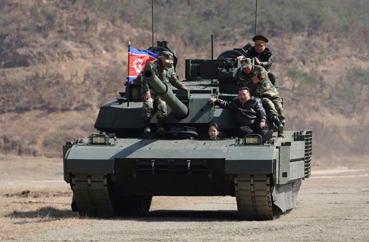 Kim Ju Ae drives a new-model North Korean tank during a combined arms tactical exercise at Pyongyang's 60th Training Base, March 19, 2026, as Kim Jong Un and military officers look on
