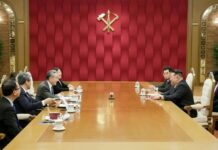 Kim Jong Un meets Chinese Foreign Minister Wang Yi at a conference table in Pyongyang, with the Workers' Party of Korea emblem on the wall behind them
