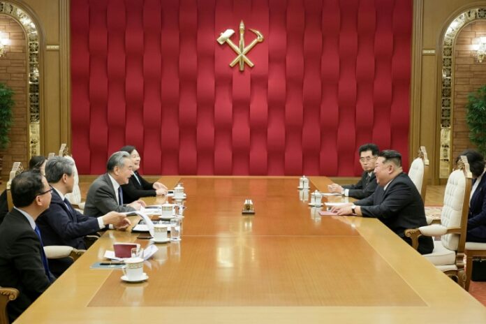 Kim Jong Un meets Chinese Foreign Minister Wang Yi at a conference table in Pyongyang, with the Workers' Party of Korea emblem on the wall behind them