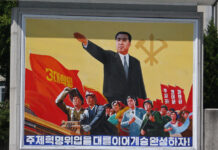 A propaganda poster in Pyongyang featuring a political figure gesturing before a crowd, red flags bearing the Three Revolutions slogan, and the WPK emblem