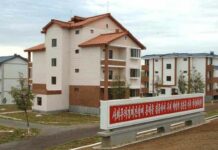 Soaring prices squeeze North Korea’s vulnerable households A newly built apartment block with red tile roofing and balconies stands among similar housing in a landscaped development, with a red propaganda sign in the foreground reading a slogan calling to concentrate efforts on socialist economic construction and accelerate the revolution's advance.