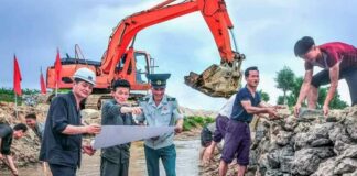 North Korea mobilizes factory workers for flood prevention push as rainy season approaches North Korean workers and a uniformed official review plans during river and embankment repair work, with an excavator operating in the background