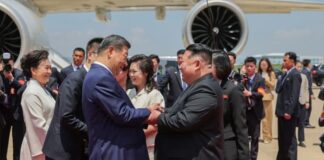 Hyesan residents see hope for economic relief in Xi Jinping’s visit Chinese President Xi Jinping and North Korean leader Kim Jong Un shake hands and clasp arms on a red carpet beside Xi's plane at Pyongyang International Airport, with Peng Liyuan and Ri Sol Ju standing nearby alongside officials and photographers.