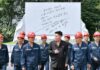 Hard-hatted miners in front of an inscribed stone monument at the 2.8 Jikdong Youth Coal Mine