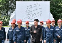 Hard-hatted miners in front of an inscribed stone monument at the 2.8 Jikdong Youth Coal Mine