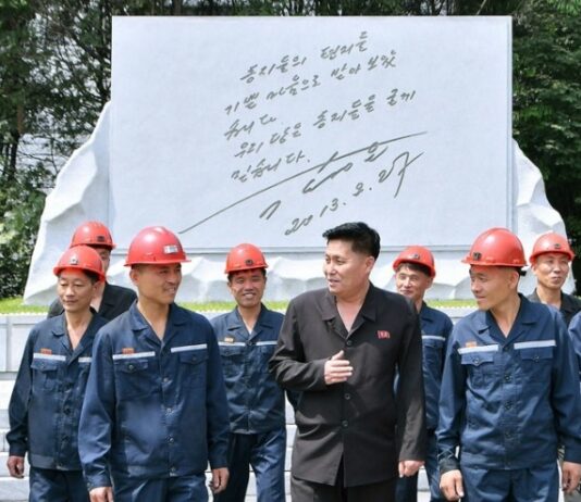 Hard-hatted miners in front of an inscribed stone monument at the 2.8 Jikdong Youth Coal Mine