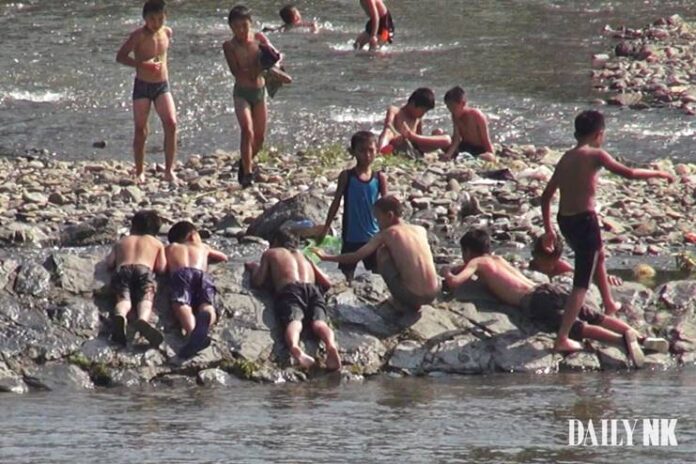 Boys swim and rest along a rocky riverbank on the Yalu River near Hyesan, Ryanggang province