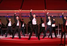 Young North Korean performers in black and white outfits dance in formation with fists raised on a red stage during the 2026 New Year Celebratory Performance at Rungrado 1st of May Stadium in Pyongyang.