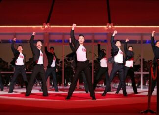 Young North Korean performers in black and white outfits dance in formation with fists raised on a red stage during the 2026 New Year Celebratory Performance at Rungrado 1st of May Stadium in Pyongyang.