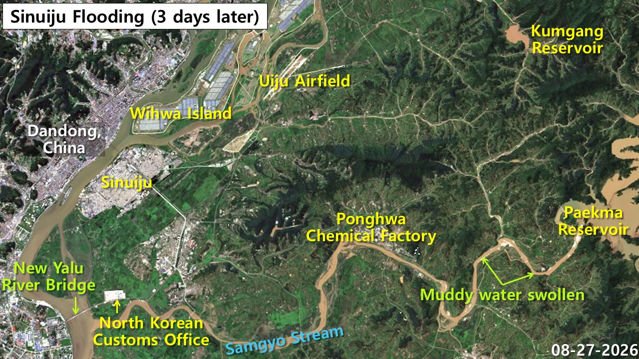Satellite optical image of Sinuiju area on Aug. 27, 2026 showing post-flood conditions with muddy water still visible in Samgyochon Stream, Uiju Airfield covered in silt, Bongwha Chemical Factory, customs office and Wihwada Island visible, comparing recovery across different protected and unprotected areas.